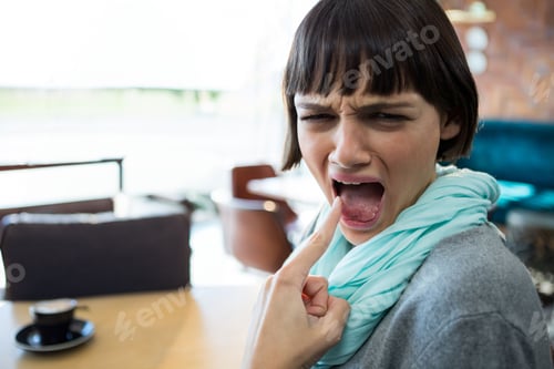 Preview: Woman in her twenties pressing finger against tongue seated at cafe table with black coffee cup