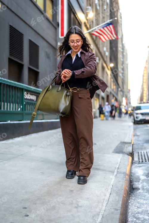 Preview: Young businesswoman checking time walking city sidewalk