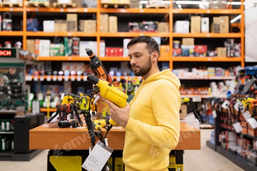 Preview: a young man compares two drills in a power tool store