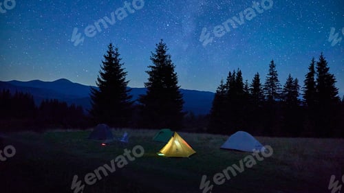 Preview: Few tents on grassy clearing under dazzling, starry sky with Milky Way clearly visible.