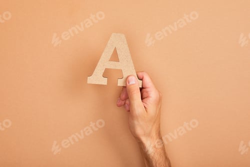Preview: cropped view of man holding paper cut letter A on beige background