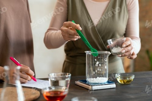 Preview: Young woman holding glassware with melted soap mass over table with glassware