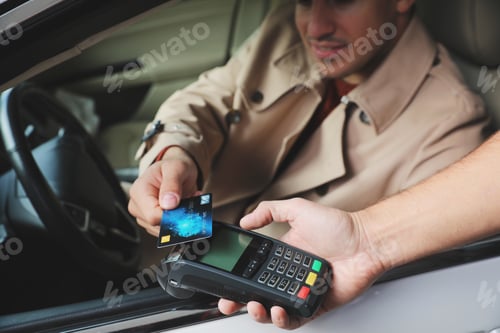Preview: Man sitting in car and paying with credit card at gas station, closeup