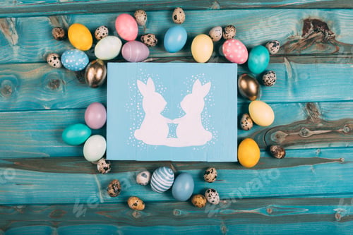 Preview: top view of colorful easter greeting card with rabbits and colorful eggs around on blue wooden