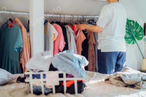 Preview: Woman selecting clothes from her wardrobe for donating to a Charity shop. Decluttering, Sorting