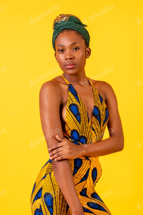 Preview: African young woman in the studio on a yellow background, portrait in a traditional costume looking
