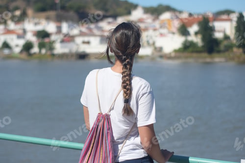 Preview: Back view of a female with a white t-shirt enjoying the view of the lake