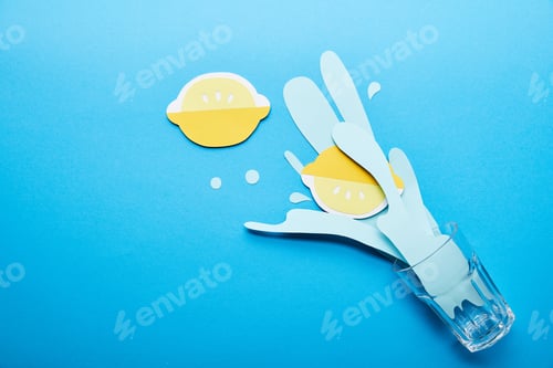 Preview: top view of glass with paper cut water splash and lemons on blue background with copy space