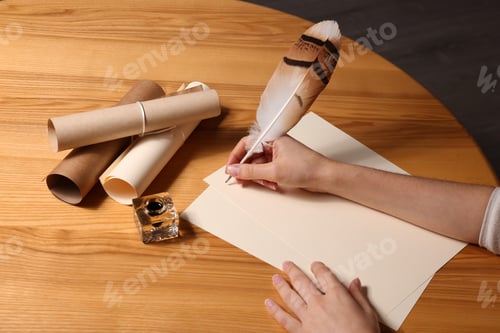 Preview: Woman using feather pen to write with ink on parchment at wooden table, closeup