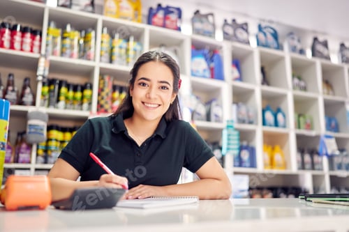 Preview: young latin saleswoman behind counter writing in a small auto parts store