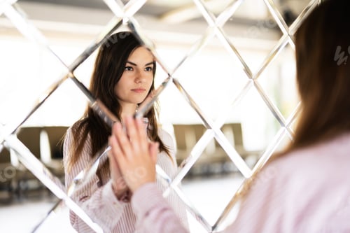 Preview: Young beautiful brunette woman in shirt touching mirror made of rhombuses.