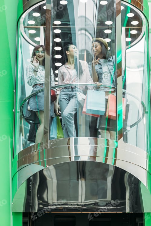 Preview: happy stylish friends with shopping bags in elevator in shopping mall
