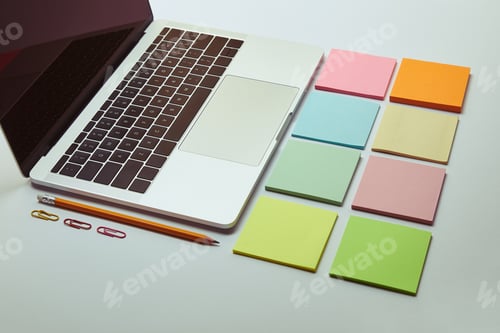 Preview: laptop, set of colored paper stickers, pencil and paper clips on white tabletop