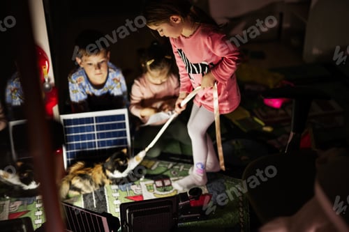 Preview: Children playing at home during a blackout using alternative lighting with solar panel.