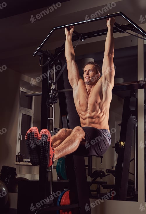 Preview: Muscular shirtless man doing push-ups on the horizontal bar in the gym.