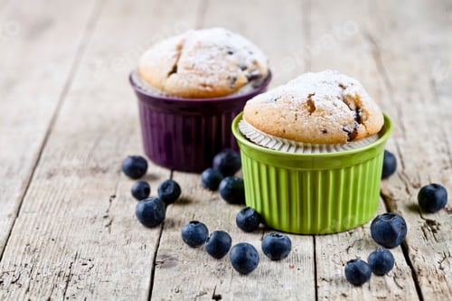 Preview: Two homemade fresh muffins on ceramic green and purple bowls with blueberries on wooden table.