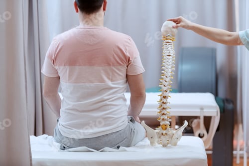 Preview: Male Patient Sitting On The Hospital Bed With Backs Turned. Next To Him Is Nurse Holding Spine