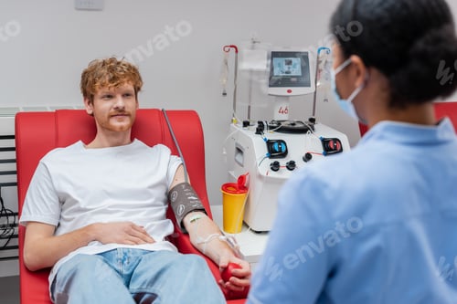 Preview: redhead man in blood pressure cuff holding rubber ball while sitting on medical chair