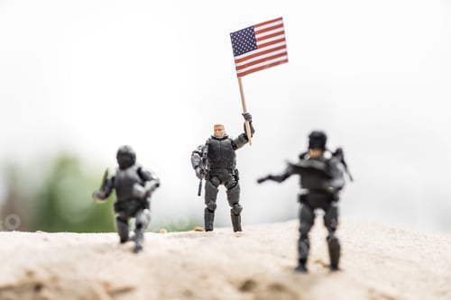 Preview: selective focus of toy soldier with weapon holding american flag on sand
