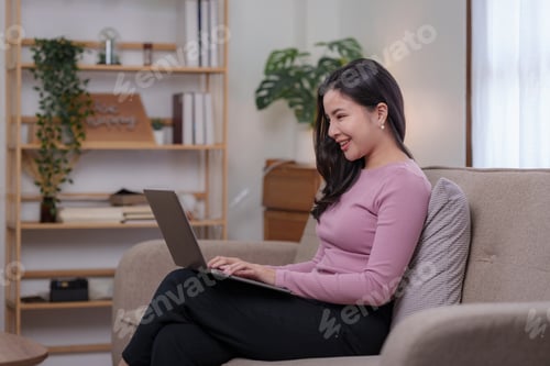Preview: Cute and bright Asian businesswoman sitting smiling happily on the sofa at home
