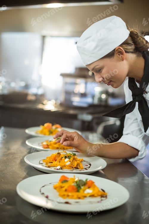 Preview: Asian female chef carefully garnishing pasta plates in commercial kitchen with tweezers, copy space