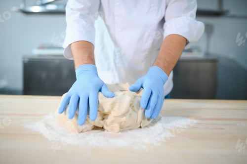Preview: Young male chef kneads dough in professional kitchen. The concept of semi-finished products