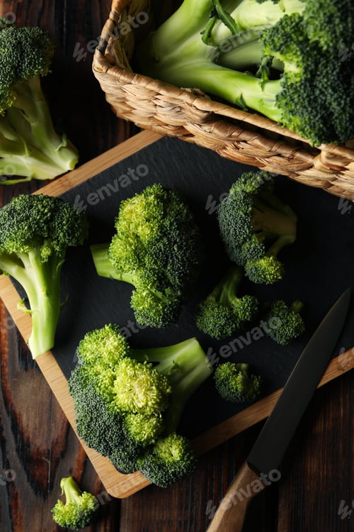 Preview: Board and basket with broccoli on wooden background, top view