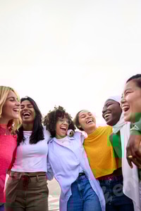Preview: Group of multiracial young only women standing embracing together in circle laughing outdoor.