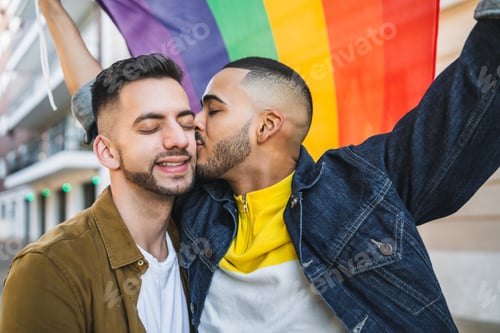 Preview: Gay couple embracing and showing their love with rainbow flag.