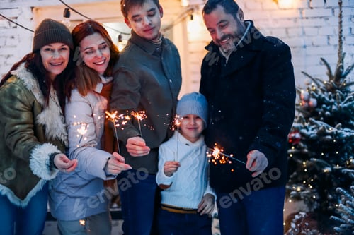Visualização: Feliz Natal. Grande família feliz em pé no quintal coberto de neve com faíscas acesas nas mãos