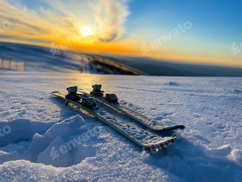 Preview: Selective focus of skis placed on the snow with the sun setting in the background