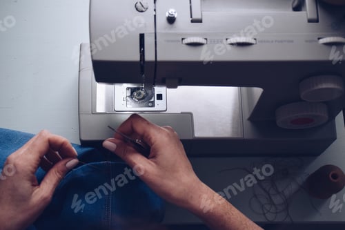 Preview: Seamstress is cutting a thread on the jeans she is hemming on sewing machine