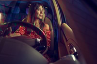 Preview: Smiling young woman driving car at night