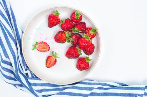 Preview: Fresh ripe red strawberry harvest on white plate and blue towel. Top view