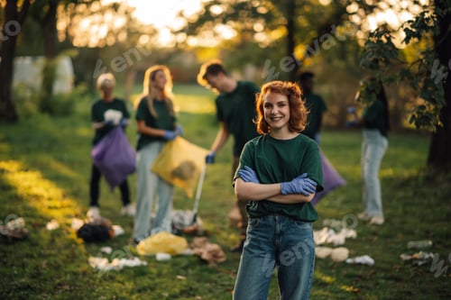 Preview: Young woman volunteer smiling with arms crossed picking up trash in park
