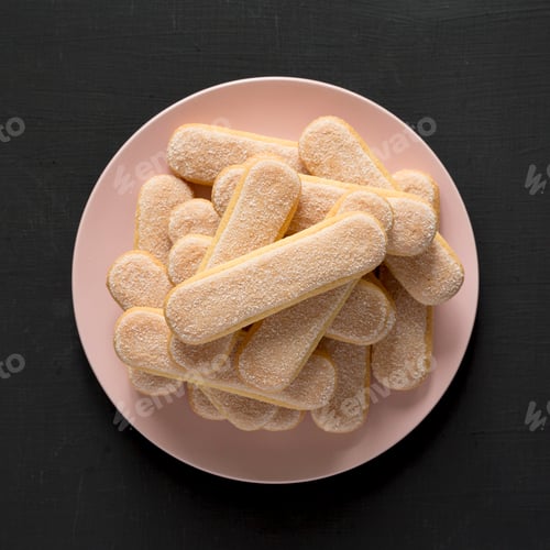 Preview: Savoiardi or ladyfingers cookies on pink plate on a black surface, top view. Overhead.