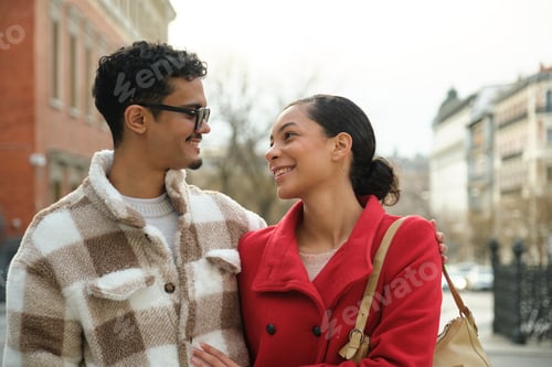Preview: Young latin couple smiling and walking arm in arm in the city