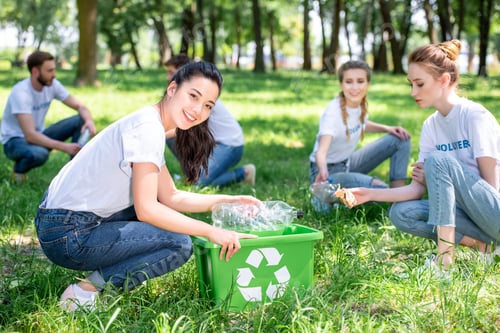 Preview: young smiling volunteers cleaning park with recycling box