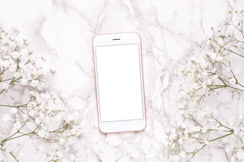 Preview: Mobile phone mock up and white flowers on marble table top view in flat lay style.