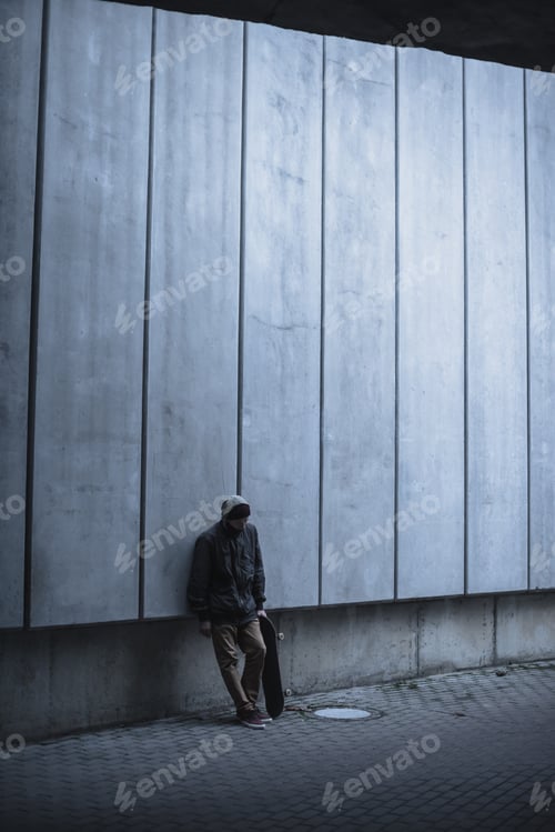 Preview: skateboarder with board leaning back on grey concrete wall