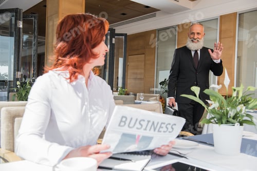 Preview: beautiful mature businesswoman waiting for meeting and reading newspaper
