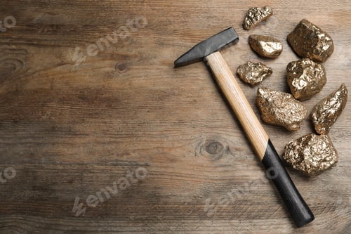 Preview: Pile of gold nuggets and hammer on wooden table, flat lay. Space for text