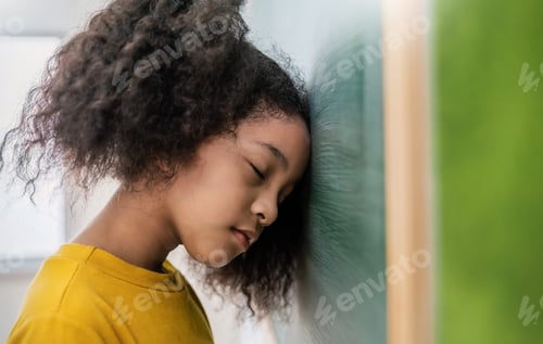 Preview: Portrait of sad little African girl lean head near the blackboard indoors