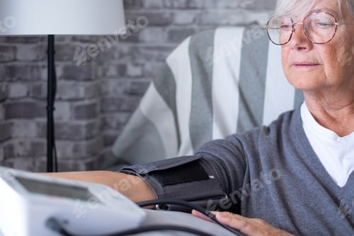 Preview: Senior woman using medical device to check measure blood pressure suffering from hypertension