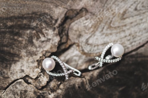 Preview: Couple wf woman earrings close up on wooden texture. Golden jewelry with pearls and diamonds