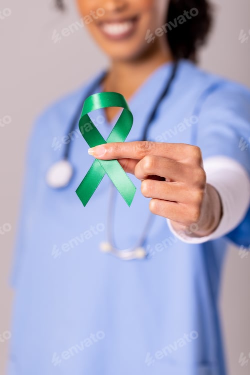 Preview: Midsection of african american mid adult female doctor holding green mental health awareness ribbon