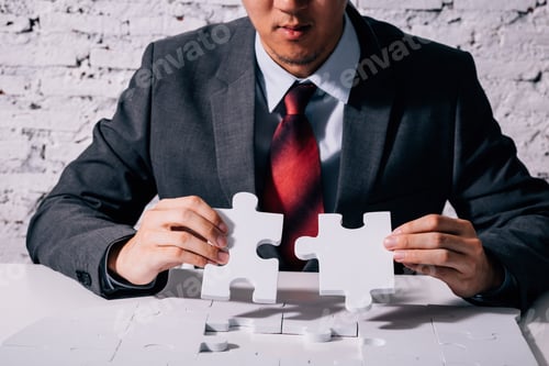 Preview: Hands of business man working on finishing last missing pieces of jigsaw