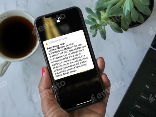 Preview: Woman holding mobile with a tornado warning emergency alert in her area indicating to take shelter