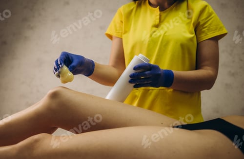 Preview: Beautician waxing female legs in spa center.
