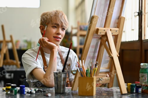 Preview: Pleased male artist looking at his artwork with admiration.
